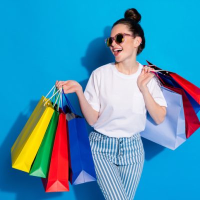 Portrait of excited cheerful positive girl enjoy leisure time hold many bags like black friday season sales wear white denim isolated over bright shine color background