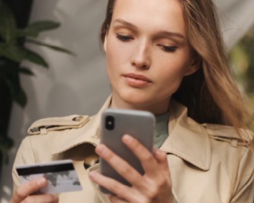 Mujer utilizando un celular y sosteniendo una tarjeta de crédito