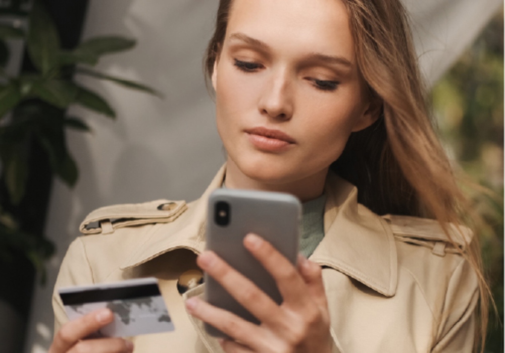 Mujer utilizando un celular y sosteniendo una tarjeta de crédito
