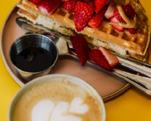 Plato de waffles con manjar y frutillas acompañado de un café