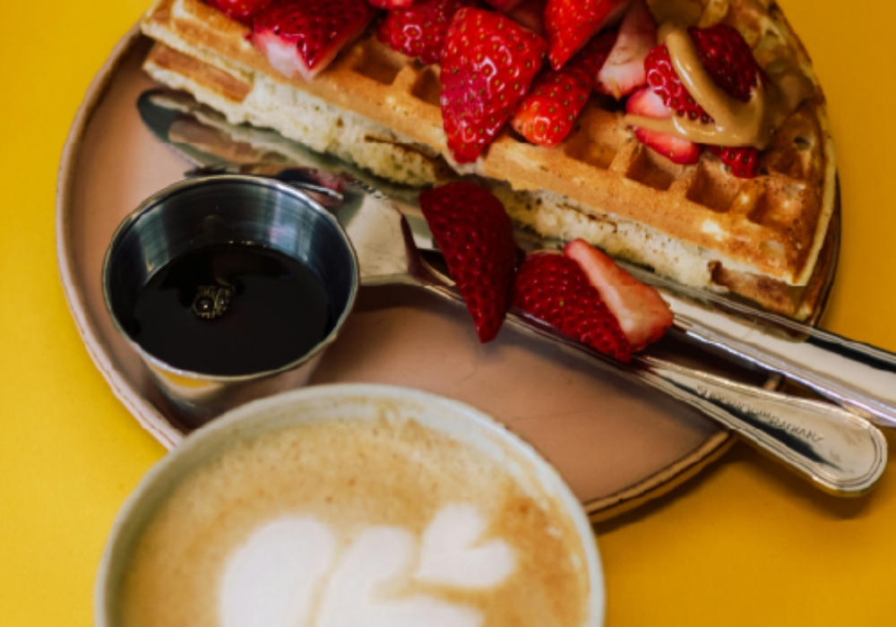 Plato de waffles con manjar y frutillas acompañado de un café